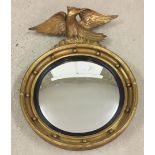 A round gilt framed convex mirror with eagle decoration approx 57cm high.