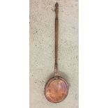 A copper bed pan with dark oak handle.