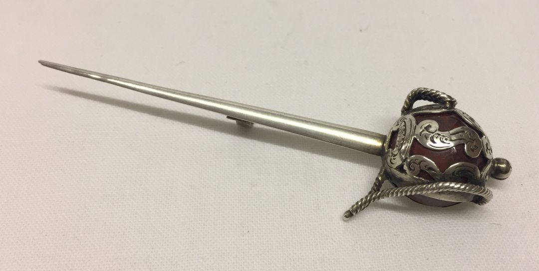 Antique basket handled sword brooch measuring 9cm long. Hilt is in white metal figure work over a