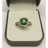 A 925 silver dress ring set with a central green stone with white stones surrounding it and on the