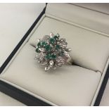 A 14ct white gold cluster ring, unusual setting with 27 diamonds and 10 emeralds. Size O, total
