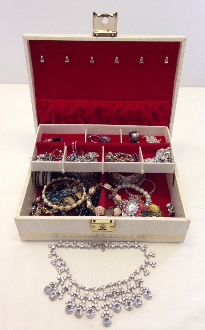 A cream jewellery box containing a collection of costume jewellery.