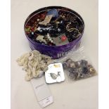 A tin of costume jewellery necklaces and rings.