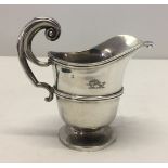 An ornate silver cream jug with engraved dolphin decoration.