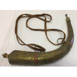 A vintage Arabic brass powder horn with leather straps.