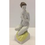 A large German porcelain figurine of a nude woman kneeling on a yellow cloth.
