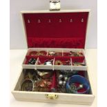 A cream jewellery box containing a quantity of costume jewellery.