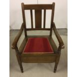 A vintage wooden commode chair with red fabric seat.