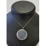 A large circular silver locket on a silver belcher chain.