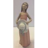 A Lladro figurine of a young girl holding a summer hat.