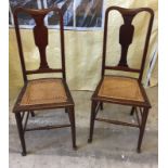 A pair of dark wood high back bedroom chairs with cane seats.