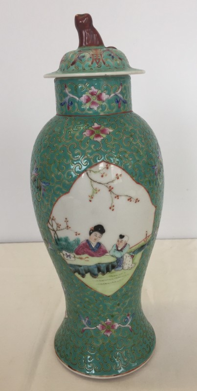 A decorative Chinese ceramic lidded jar with painted panels on a turquoise background.