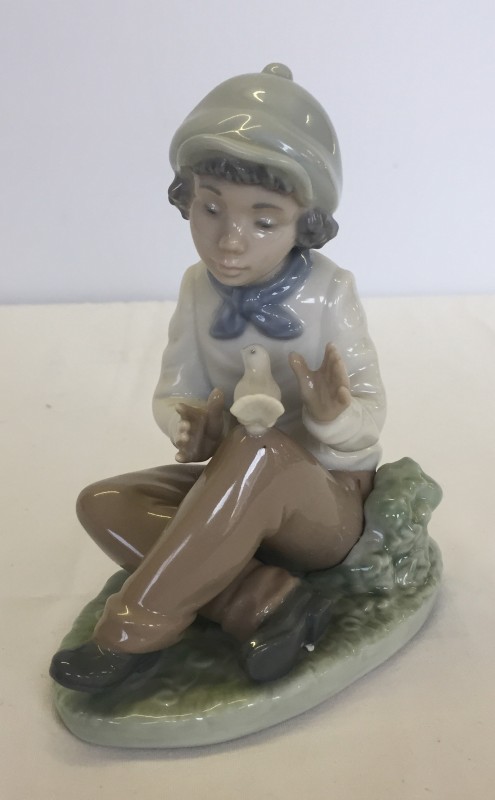 A boxed Nao porcelain figurine of a boy sitting with a dove.