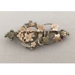 A silver sweetheart brooch decorated with gold and rose gold flower and leaf pattern.