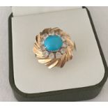 Ladies gold dress ring set with a turquoise cabochon stone surrounded by clear stones.