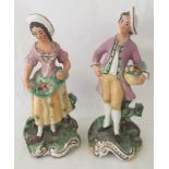 A pair of Victorian ceramic figurines of a man and woman holding baskets of fruit.