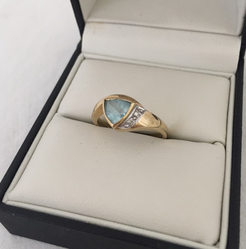 A 9ct gold dress ring set with triangular shaped blue topaz and 2 small diamonds.