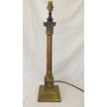 A brass column style lamp base with orange lamp shade.
