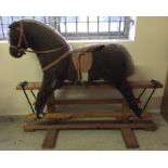 A large brown furred rocking horse with saddle on swing stand.