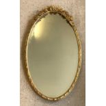 An oval gilt framed mirror with floral design to top.