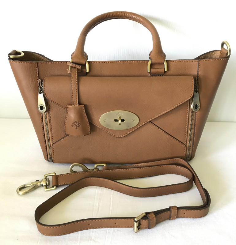 An unused brown leather handbag with detachable shoulder strap and dust cover.