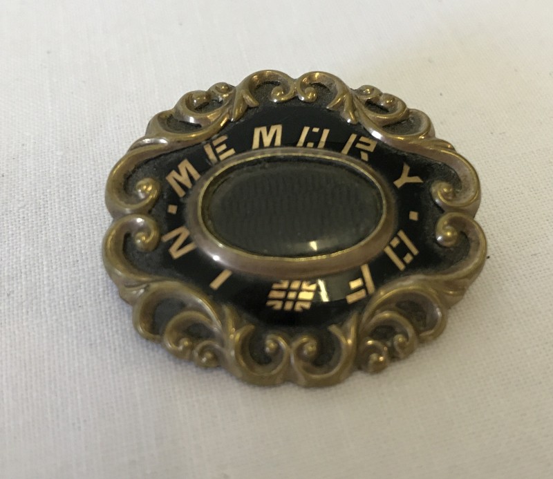 A vintage decorative mourning brooch with central glass panel.