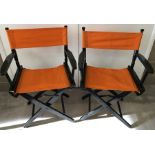 2 folding wooden directors style chairs with orange fabric seats.