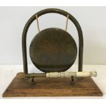 A vintage brass gong on a wooden mount with a decorative horn handled beater.