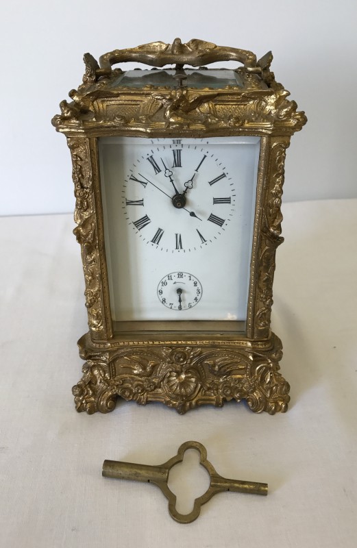 An ornate repeating carriage clock with enamel face and bevel edge glass panels.