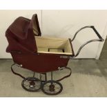 A vintage maroon coloured dolls pram.