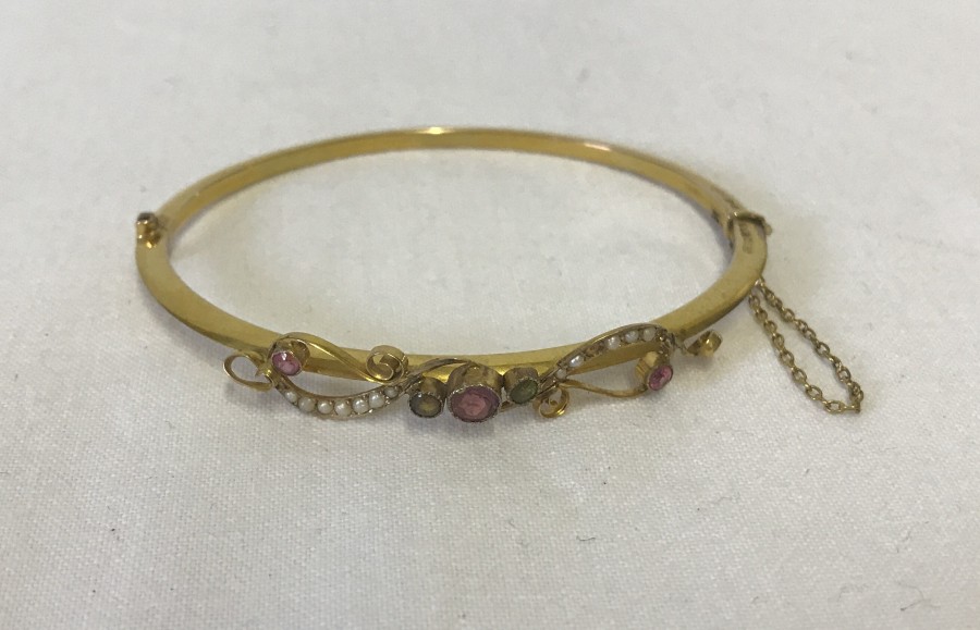 A 9ct gold hinged bangle set with pink and green coloured stones and tiny seed pearls.