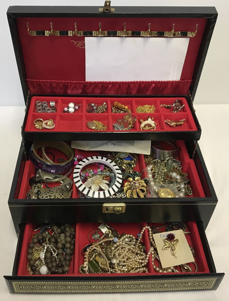 A large black & gold jewellery box with 2 trays containing many items of costume jewellery & badges.