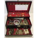 A large black & gold jewellery box with 2 trays containing many items of costume jewellery & badges.