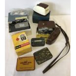 A box of vintage cameras and equipment with vintage tins.