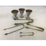 3 silver plated egg cups together with 4 pairs of silver plated sugar tongs.