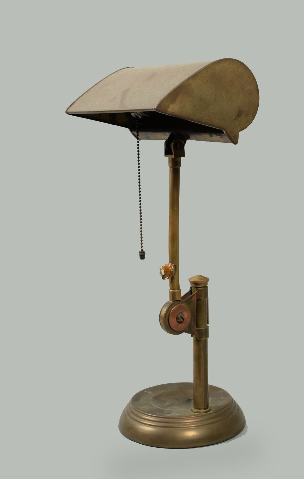An early 20c brass desk lamp, adjustable and with shades, supported on a circular dished base, 18h.