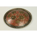 An 18c Indian Dhal with four studs, red and black decorated with leaf and scrollwork, 10.5diam.