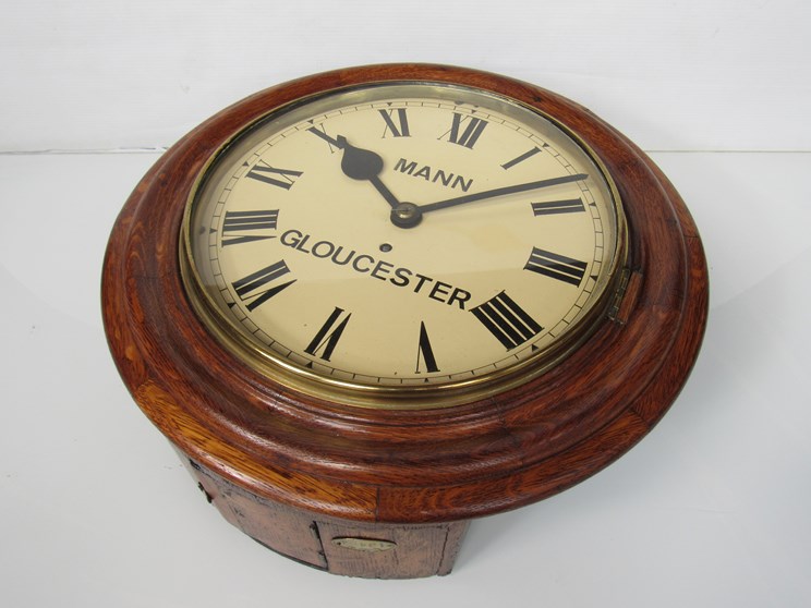 An oak station dial clock, Roman painted metal dial signed Mann, Gloucester, chain fusee movement,