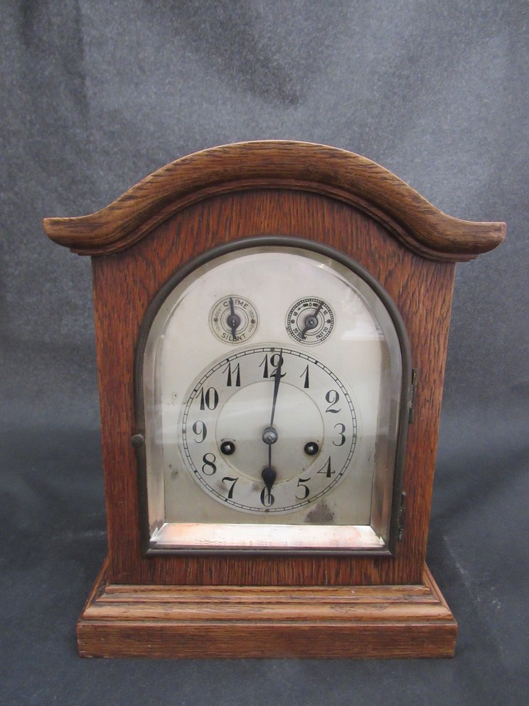 An oak cased dome top mantel clock with arched silvered dial,