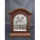 An oak cased dome top mantel clock with arched silvered dial,