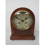 An oak cased domed mantel clock with carved panel and bun feet, Arabic silvered dial,
