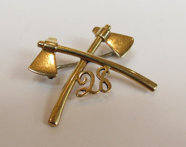 A yellow metal crossed axes military badge with No.