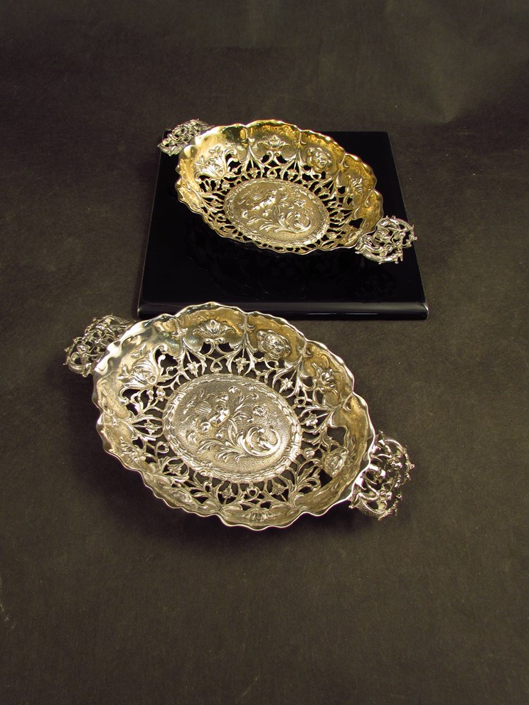 A near pair of William Comyns bon-bon dishes with embossed and floral detail, twin cherub handles,