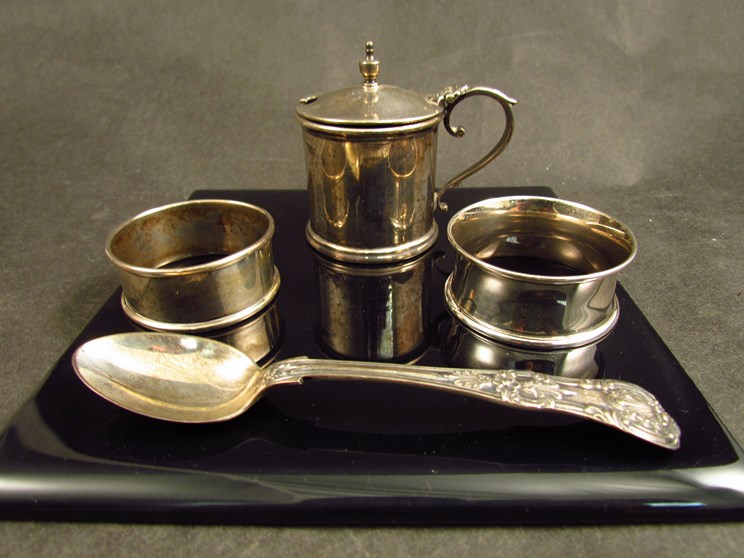 A group of silver items including two napkin rings, a mustard pot and spoons,