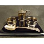 A group of silver items including two napkin rings, a mustard pot and spoons,