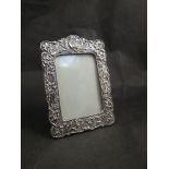 A silver easel back photograph frame, foliate detail,