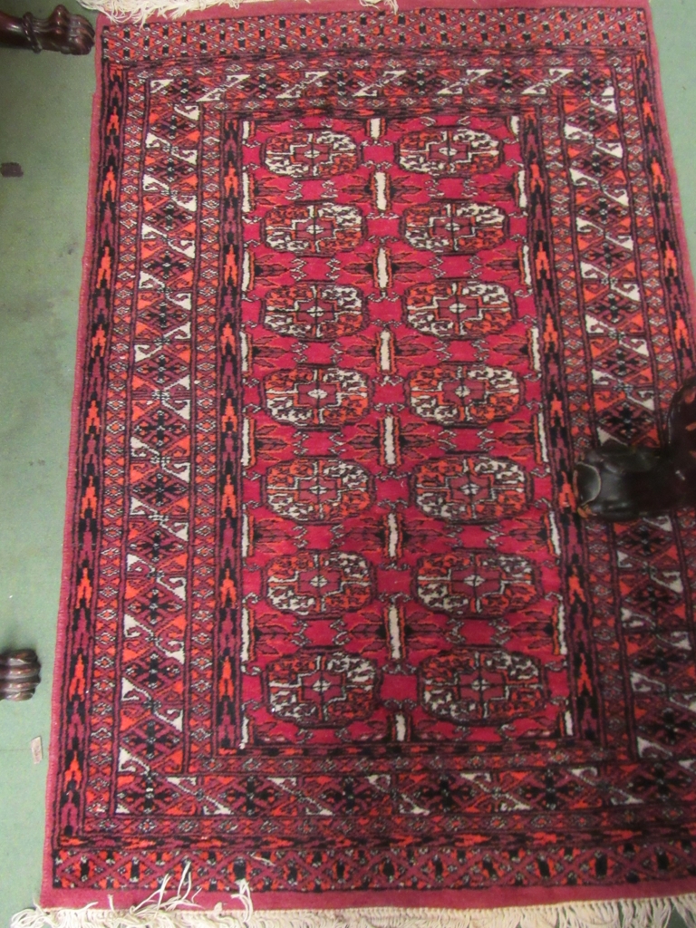 A red ground rug with geometric design and tasselled ends,