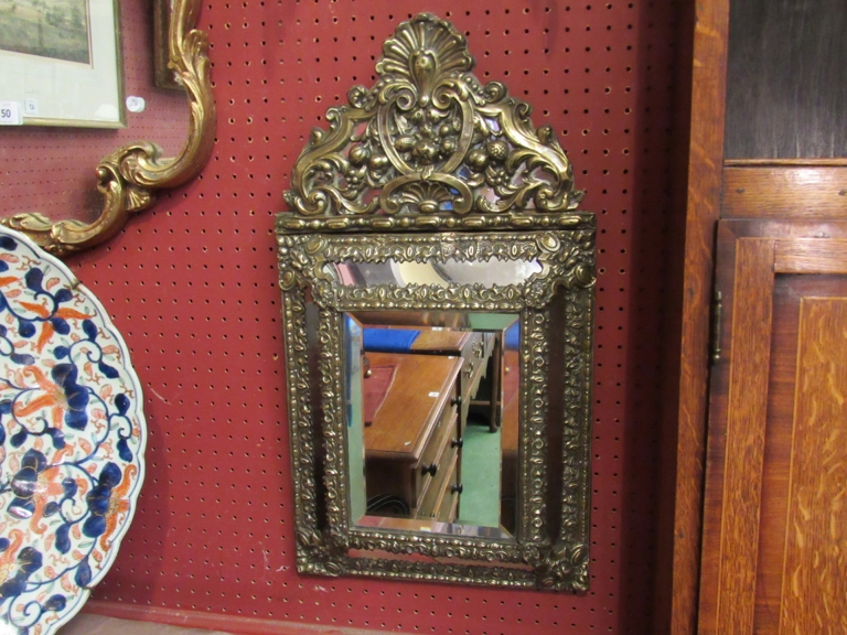 A 16th Century Style brass embossed cushion mirror with scroll,