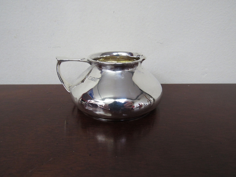 A silver cream jug of squat form, London, gilded interior, dented,