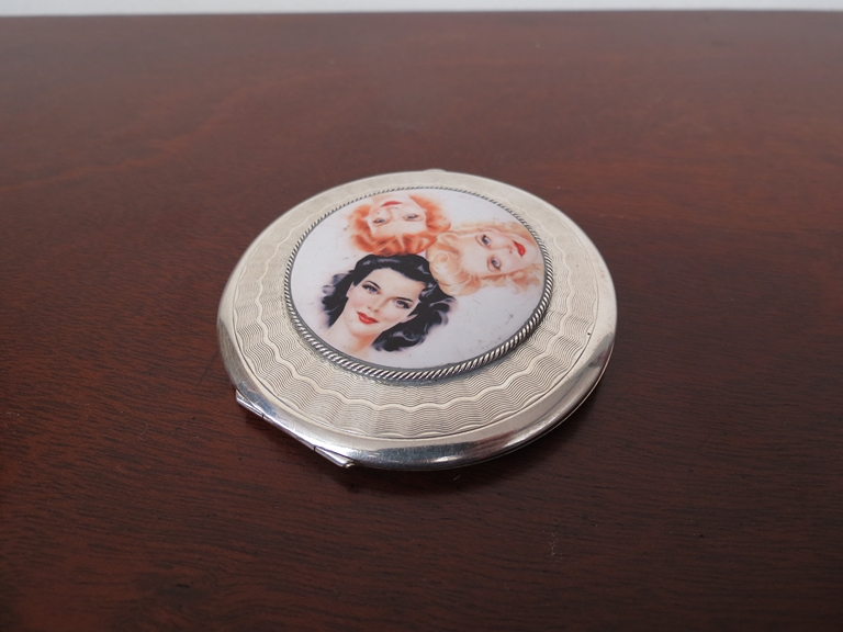 A silver compact with engine turned detail set with later porcelain plaque depicting three female